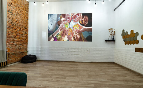 Арендовать Rubin Loft (Рубин Лофт). Лофт средний. Просторная комната с деревянным полом и кирпичной стеной. Белые стены с проектором, деревянные панели. Черные подвесные светильники, зеленое кресло, черный пуф, настенная полка с декором и шестиугольные украшения.