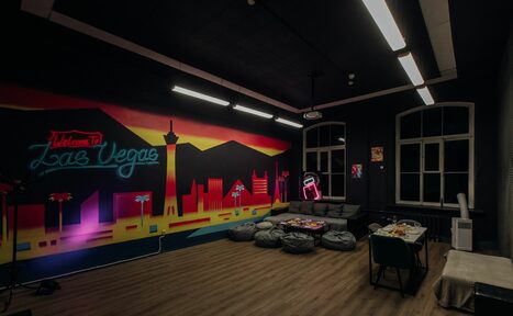 Арендовать Rubin Loft (Рубин Лофт). Зал Лас-вегас. Арт-пространство с неоновым граффити на стене. Небольшие мягкие кресла и столы с закусками. Диван, стулья, длинные потолочные светильники. Темный потолок, деревянный пол, большие окна. Настенное искусство с городским пейзажем и неоновые вывески.