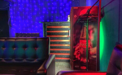 Арендовать Rave(Рейв). Кожаные диваны, небольшой бар с черно-красной полосатой отделкой, автомат с напитками, яркие разноцветные светодиоды на стене, мягкое освещение.