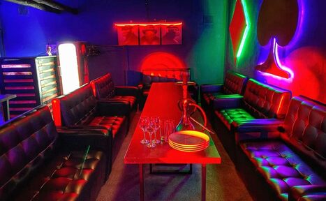 Арендовать Rave(Рейв). Караоке-зал с красной мебелью: длинный стол, кожаные диваны. На столе стеклянная посуда и кальян. Неоновое освещение в виде карточных мастей. Стены темные. Наличие холодильника. Настенное изображение из трех сегментов.