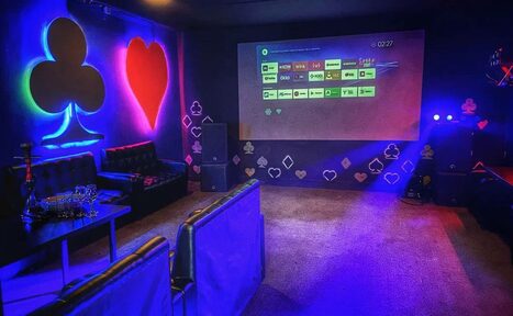 Арендовать Rave(Рейв). Частная комната с черными диванами, кофейным столиком с кальяном и проектором на стене. Декор в виде светящихся клубов и сердец на темных стенах. Пол покрыт ковролином. Освещение неоновое, разноцветное.