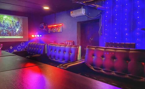 Арендовать Rave(Рейв). Караоке-зал с кожаными диванами, столами, проектором на стене. Синие стены с неоновыми огнями, светодиодные гирлянды. Потолок с точечными светильниками, кондиционер на стене. Преимущественно темные цвета, акценты красного и синего освещения.