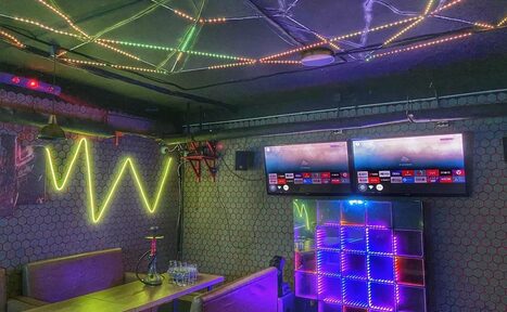 Арендовать Bee-lounge(Пчела-лаундж). Караоке-зал с двумя телевизорами на стене, рядом стол с диваном. На стенах и потолке светодиодные ленты разных цветов, неоновая надпись, шестигранная плитка. На столе стеклянные стаканы и кальян. Освещение разноцветное.