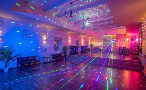 Арендовать Loft Lodge (Лофт Лодж) 7. Просторный уютный лофт. Просторное помещение с деревянным полом, кирпичными стенами, освещённое разноцветными лазерами и диско-шаром. На стене часы, по периметру растения в горшках, мягкая мебель и столики. Потолок украшен светильниками.