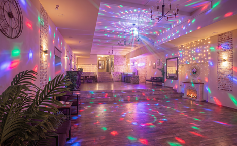 Арендовать Loft Lodge (Лофт Лодж) 7. Просторный уютный лофт. Большое пространство с деревянным полом и кирпичными стенами. На потолке светящиеся гирлянды и диско-шар, проецирующий разноцветные огни. Есть декоративный камин, столы, стулья, зелёные растения и неоновая вывеска. Висит настенные часы.