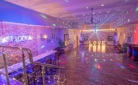 Арендовать Loft Lodge (Лофт Лодж) 7. Просторный уютный лофт. Просторное современное помещение с барной стойкой, стульями и деревянным полом. Мягкое разноцветное освещение, неоновая вывеска на кирпичной стене и большие светящиеся буквы "LOVE". Лестница с металлическими перилами, висячие светильники и декорированные растения.
