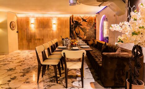 Арендовать Стильный лофт Джаванди. Элегантное пространство с большим прямоугольным столом, обставленным стульями и мягким диваном. Мраморный пол, потолочные светильники, деревянная стена с подсветкой. Украшение из белых цветов и настенное искусство. Светлая и уютная обстановка.