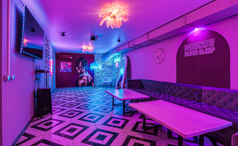 Арендовать Неоновый лофт Гламур. Пространство с неоновым освещением, деревянные столы, угловой диван вдоль стены. Пол с геометрическим узором, настенная графика и плакаты, надпись "Moscow never sleep", зеркало, телевизор, декоративное освещение.