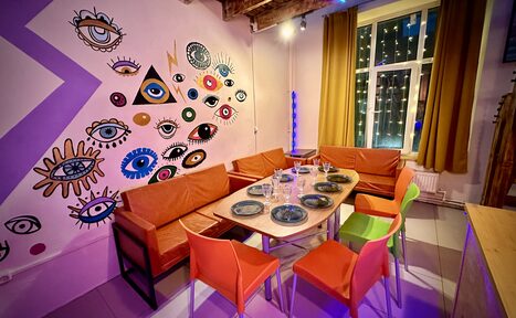 Арендовать Яркий двухуровневый лофт. Стол с посудой. Яркие стулья с диванами. Обклеенные рисунками стена. Окно с навешенной гирляндой