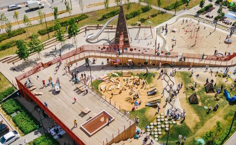 Арендовать Площадка в Москве c одной фотографией!. На изображении показана большая детская площадка с различными игровыми элементами, такими как горка, песочница и лазалки. Имеется деревянная терраса и мостики. Люди гуляют и играют на территории.