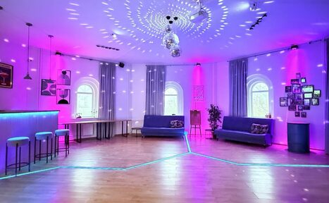 Арендовать Центрум. Уютное светлое пространство круглой формы. Просторное помещение с деревянным полом и несколькими арочными окнами, обставленное серыми диванами и барной стойкой с высокими стульями. Разноцветное подсвечивание, зеркальные шары на потолке, декоративные растения и фоторамки на стене.