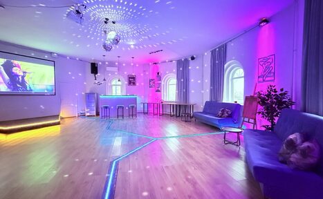 Арендовать Центрум. Уютное светлое пространство круглой формы. Просторное помещение с деревянным полом, несколькими диванами и барной стойкой. На стене экран с проектором. Праздничное освещение с диско-шаром и цветными светодиодами. Высокие окна с арками и занавесками. На стенах постеры и растения.