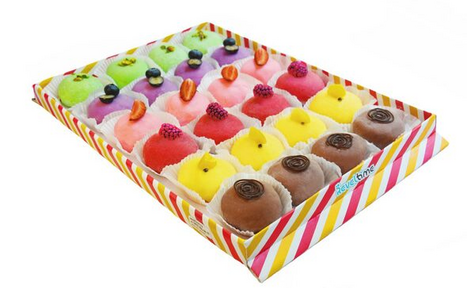 Арендовать Тестовый зал. Изображены разноцветные десерты в картонной коробке, выложенные рядами по четыре. Цукаты, орехи и глазурь украшают кремовые пирожные. Коробка белая с разноцветными полосами.