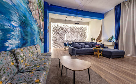 Арендовать Rubin Loft (Рубин Лофт). Зал Сицилия. Просторное помещение с диванами, обеденной зоной и стульями. Стены отделаны текстурированными панелями и росписью. Потолочные светильники. Пол деревянный, на полу коврики. Шторы темно-синие, декоративная зелень.