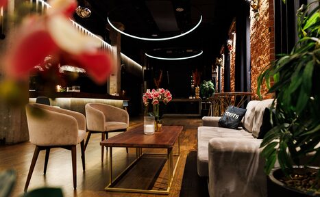 Арендовать Двухуровневая event-площадка 550 м². Современное помещение с диванами и креслами, деревянным столом, мягким освещением. На столе ваза с цветами. Стены из красного кирпича и деревозаменителя. Потолочные светильники круглой формы. Планировка открытая, полы деревянные.