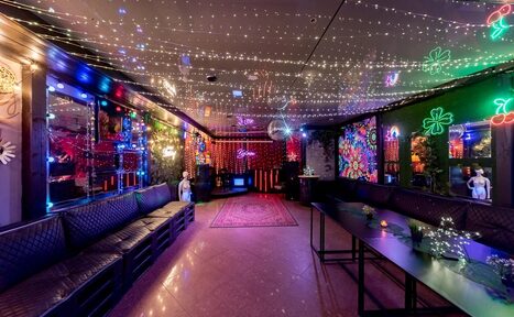 Арендовать Яркий лофт для праздников. Просторное помещение с длинными диванами вдоль стен, низкими столами и цветными неоновыми украшениями на стенах. Потолок украшен множеством маленьких светодиодов. Пол гладкий, с розовым ковром. Зеркала на стенах, приглушенное освещение.