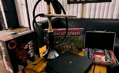 Арендовать Лофт-мансарда . Комната с чёрным диваном, деревянным журнальным столиком, на котором находится кальян, настольные игры "Мафия" и "Монополия", чемодан с покерными фишками. Стены отделаны белыми панелями.