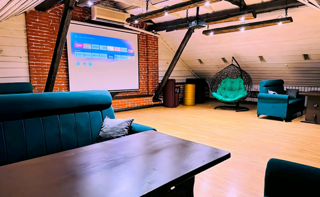 Арендовать Лофт-мансарда . Лофт-пространство с деревянным полом и кирпичными стенами. Присутствует проектор с экраном, диваны и кресло-качалка зелёного цвета. Используются подвесные лампы. Потолок с белыми панелями, балки окрашены в тёмный цвет.