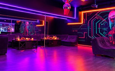 Арендовать Cyberpunk (Киберпанк). Темное помещение с неоновым освещением. По периметру мягкие диваны. На стенах граффити в стиле киберпанк. В центре металлический шест. Столы с напитками и свечами. Зеркала на стенах. Пол – деревянный. Атмосферное освещение.
