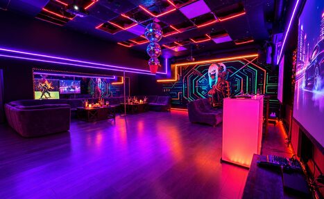 Арендовать Cyberpunk (Киберпанк). Клубное пространство с неоновым освещением, мягкой мебелью у стен, зеркалами, экраном, деревянным полом, столиками и баром. Декор в виде диско-шаров и графического настенного рисунка. Цвета: фиолетовый, розовый, синий.