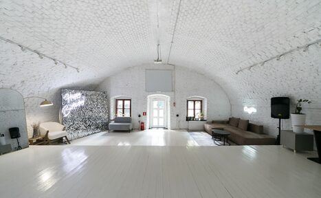 Арендовать Brodniki Loft (Бродники Лофт). Лофт из белого кирпича. Арочное помещение с белыми кирпичными стенами и деревянным полом. В центре диваны, кресло, столики, торшер. На стене неоновая надпись. Трековое освещение. Деревянные окна, дверь, вазы с растениями. Пространство минималистично оформлено.