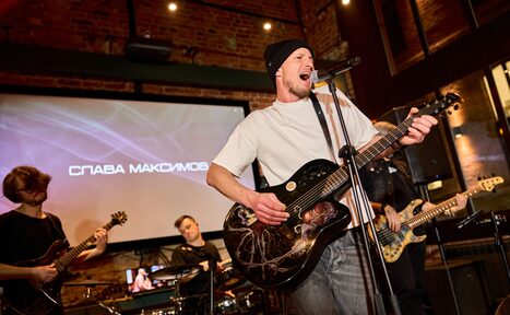 Арендовать Лофт для мероприятий с гольф-симулятором. Пространство для музыкальных выступлений; кирпичные стены; группа музыкантов с гитарами и барабанами; проектор с экраном, показывающим текст; система освещения точечного типа; деревянные элементы интерьера; темные и теплые тона.