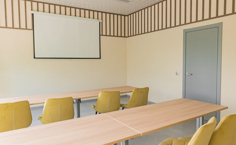 Арендовать Зал 5. Светлый малый конференц-зал до 20 человек в Академии Кантаты. Просторное помещение с бежевыми стенами; серый дверной проем. Продолговатые светлые деревянные столы, вокруг которых расположены желтые стулья на колесиках. На стене установлен белый экран для проекции. Потолок оформлен светлыми панелями и деревянными рейками.