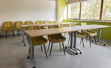 Арендовать Зал 5. Светлый малый конференц-зал до 20 человек в Академии Кантаты. Учебное пространство с двумя столами на колесах и стульями приятного жёлто-зелёного цвета с мягкими сиденьями. Большое окно с бежевой шторой пропускает естественное свет. Пол из светлого материала, стены белые и салатовые.