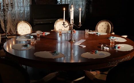 Арендовать Polygon(Полигон). Зал Апартаменты. Круглый деревянный стол с подсвечником на три свечи. Вокруг стола расположены стулья с мягкой обивкой. На столе разложены карточки, фишки и бокалы с напитками. Фон затемнён, видны свечи и занавески.