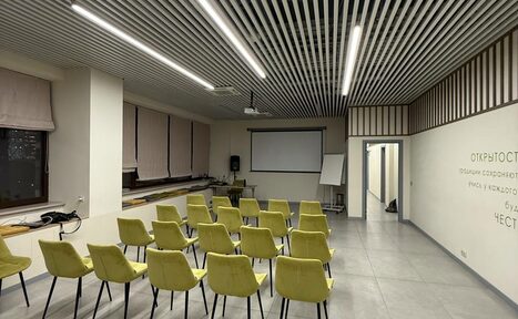 Арендовать Зал 6. Просторный и светлый конференц-зал до 50 человек в Академии Кантаты. Просторное помещение с проектором и экраном, светло-зелёные стулья в несколько рядов, светло-серые плиточные полы, подвесной белый потолок с ламелями, белые стены с текстом. Настенные светильники, флипчарт у стены.