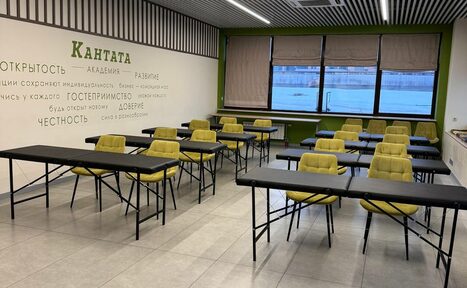 Арендовать Зал 6. Просторный и светлый конференц-зал до 50 человек в Академии Кантаты. Аудитория с рядами черных столов и желтыми стульями. На стене текст с надписью "КАНТАТА". Окно с видом на воду; жалюзи. Потолок с ламелями и встроенными светильниками. Светлая плитка на полу.