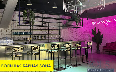 Арендовать Солист лофт | Solist loft - яркая площадка на Лиговском. Барная зона с высоким длинным столом, за которым расположены стулья с черно-белой обивкой. Зона освещена неоновыми светильниками, стены окрашены в белый и розовый цвета. На заднем плане виднеется красный диван и растения. Над столом металлические конструкции с растениями. Текст: «БОЛЬШАЯ БАРНАЯ ЗОНА», «SOLIST KARAOKE LOFT».