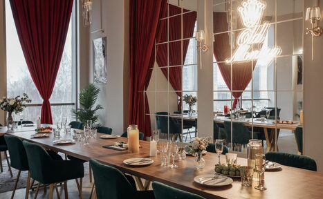 Арендовать Rubin Loft (Рубин Лофт). Зал Олд Мани. Большое помещение с длинным деревянным столом, окруженным мягкими стульями. На столе посуда и декор. Зеркальные стены с красными шторами и надпись в неоне. Естественное освещение из высоких окон. Декоративные растения.