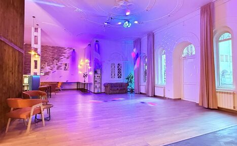 Арендовать Лофт Софт. Просторный зал с деревянным полом и высокими потолками. Стены белые с декоративными элементами. Освещение разноцветное, мягкое. По периметру стоят стулья и диваны. Есть арочные окна с занавесками. На стенах декор из кирпича и зеркала.