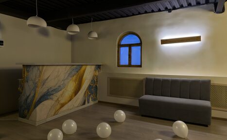 Арендовать Maybe Loft (Мэйби Лофт). Зал Olive (Олив). Современный дизайнерский лофт . Помещение с барной стойкой с абстрактным узором, рядом серая диванная скамья. Потолок декорирован подвесными светильниками. На полу разбросаны белые шары. Стена бежевого цвета с арочным окном и светодиодной панелью.