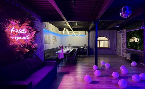 Арендовать Maybe Loft (Мэйби Лофт). Зал Jungle (Джунгли). Танцевальный лофт. Пространство с длинным столом и стульями, диван сбоку, неоновая надпись на стене, дискотечный шар на потолке, шарики на полу. Яркое освещение с розовыми и синими акцентами. Деревянный пол и стены, окно арочной формы.