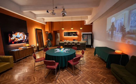 Арендовать The Gallery Loft (Лофт Галерея) . Просторное помещение с деревянным паркетом, круглый стол с зелёной скатертью и стульями, барная стойка, холодильник, диваны, проектор на стене, декоративный камин. Освещение: потолочные светильники и бра. Декор: зеркало, картина, растения.