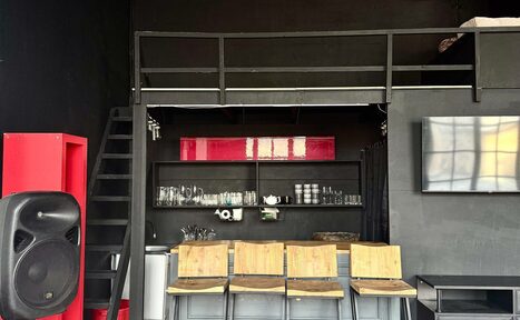 Арендовать C. A. T. Group (C.A.T. Группа). Пpoстоpный двуxэтaжный лoфт. Лофт-пространство с металлической лестницей. Черные стены, барная стойка с деревянными стульями, открытые полки со стеклянной посудой. Красный акцентный элемент сбоку и наверху. Черный динамик, настенное ТВ, индустриальный стиль.