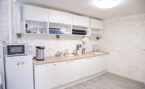 Арендовать Лофт Облака. Зал Баунти на Сельскохозяйственной. Кухонное пространство с длинной рабочей поверхностью, белыми напольными и навесными шкафами. Имеется холодильник, микроволновая печь, электрический чайник и сушилка для посуды. Светлые стены, плиточный пол, круглый потолочный светильник.