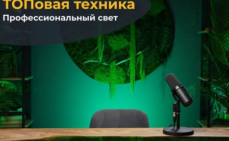 Арендовать Лофт Восторг. Общий вид стола с деревянной поверхностью, на котором стоит микрофон. За стулом серая обивка. На стене зелёная растительность в круглом панно. Слева видна полка с растениями. Освещение зелёного цвета. Текст: "ТОПовая техника. Профессиональный свет".