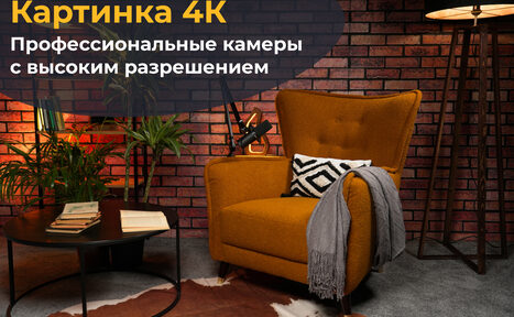 Арендовать Лофт Позитив. Современная гостиная: кирпичная стена, оранжевое кресло с подушкой и пледом, кофейный столик с книгами, напольная лампа, коврик, растения. Тёплое освещение. Текст: "Картинка 4К. Профессиональные камеры с высоким разрешением".