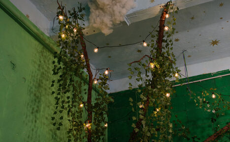 Арендовать Хендмейдщики. Лофт в лесной тематике. Зелёные стены с искусственными лианами и маленькими лампочками на потолке, украшенном звёздами. Потолок белого цвета, на нём видны текстурные элементы, напоминающие облака. Состояние хорошее, освещение атмосферное.