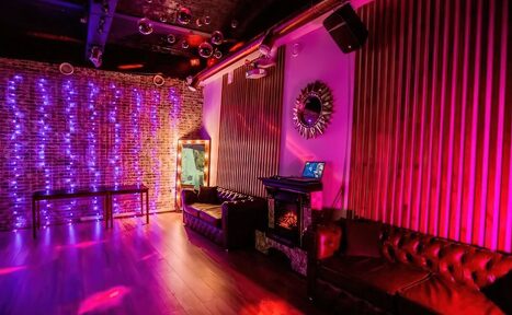 Арендовать LoftForParty. Бэкстейдж лофт . Лофт с кирпичными стенами и деревянным полом, оборудованный кожаными диванами. Освещение разноцветное, присутствуют неоновые гирлянды. На стене зеркало с декоративной рамой. Звуковое оборудование и ноутбук. Стены частично обшиты деревянными панелями.