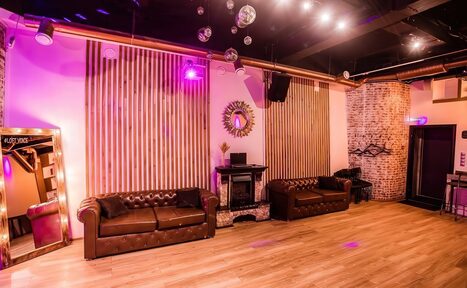 Арендовать LoftForParty. Бэкстейдж лофт . Просторное помещение с деревянным полом и кирпичной стеной. Два кожаных дивана, зеркало, декоративный камин. Потолочные светильники и неоновое освещение. Подвесные шары на потолке. Стены украшены деревянными панелями и круглым зеркалом.