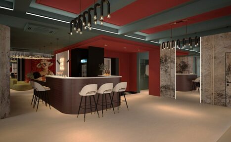 Арендовать Стильное пространство Астрид. Угловой бар с белой стойкой и пятью высокими белыми стульями с черными ножками. На потолке подвесные светильники с лампами накаливания, стены бордовые и серые с зеркалами. На заднем плане полки с напитками. Потолок синие и красные панели.