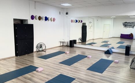 Арендовать Территория Танца. Просторный светлый зал с деревянным полом, большими зеркалами на стене и высоким потолком. Организованы коврики и блоки для йоги. На стене висят барабаны в чехлах. Присутствуют вентиляторы и черные колонки. Белые стены, дверной проем.