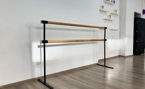 Арендовать Территория Танца. Зал с балетным станком на светло-коричневом ламинате. Белая стена с текстурой и открытыми полками с кубками. Чёрная мебель или оборудование у стены. Естественное освещение. Электрическая розетка на стене.