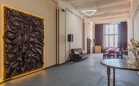 Арендовать Chocolate Loft (Шоколад Лофт). Зал с видом на Финский залив. Просторное помещение с высокими потолками, длинный стол с красным текстилем и стульями, диван, деревянный пол. Светлый потолок, стены с декоративной тканью в подсветке. Вертикальные окна с занавесками, треугольные светильники, дополнительные источники света на потолке.