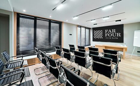 Арендовать FarFour (ФарФор). Конференц-зал. Конференц-зал с рядами черных кресел на металлокаркасе, светлые деревянные полы, белая доска, деревянный стол на подиуме, окна с жалюзи, встроенное потолочное освещение, на стене надпись «FAR FOUR inn & Suite».