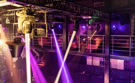 Арендовать Castle Concert Hall(Концертный зал Замок). Клубное пространство с балконом, оборудованное софитами и прожекторами. Диваны красного цвета вдоль стен, металлические перила на втором уровне. Многоцветное освещение, включая фиолетовые и розовые лучи. Потолочные конструкции и сцена.